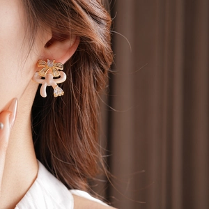 Detail of golden bow earring with cream enamel and zircon on a model ear