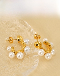 Detail of gold C-shaped hoop earrings with embedded white pearls on a satin fabric