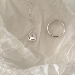 Detail of silver heart necklace with pink and green stones and a simple band ring