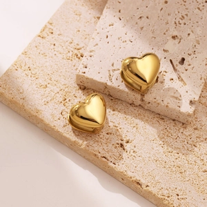 Macro shot of polished 18k gold heart huggie earrings on a textured travertine stone