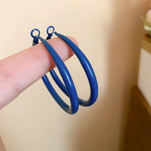 Close-up of matte Klein blue hoop earrings hanging on finger with metal texture