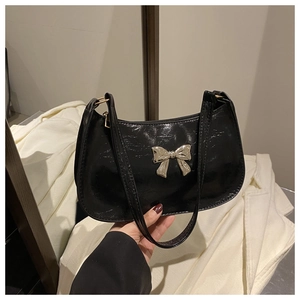 Detail of black glossy crescent shoulder bag featuring a silver metal butterfly buckle