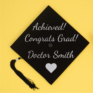 Close-up of silver glitter letter stickers on a black graduation cap with tassel