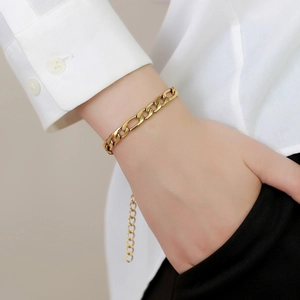 Detail of a gold Figaro link bracelet with adjustable chain on a model's wrist