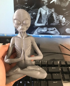 Macro shot of grey 3D printed meditating alien resin statue on a computer desk