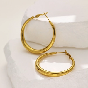 Close-up of chunky gold hoop earrings with a polished finish on a white stone background