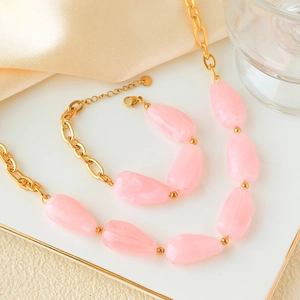 Detail of pink stone necklace and bracelet set on a white tray with gold chains