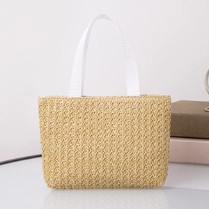 Detail of handwoven straw tote bag with white ribbon handles on a glass surface