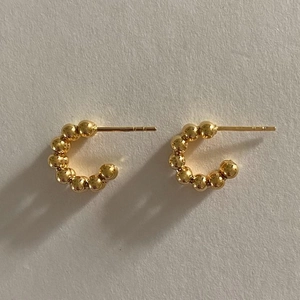 Polierte goldene Perlenohrringe in C-Form auf strukturiertem beigem Papier Schmuck