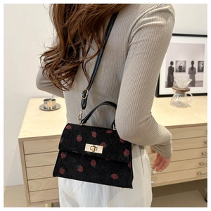 Detailed view of black corduroy handbag with red strawberry pattern and golden lock
