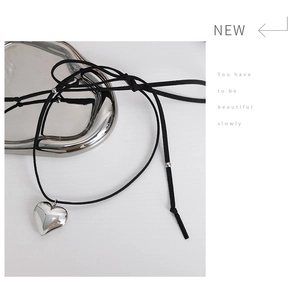 Close-up of minimalist black suede necklace with polished silver heart pendant on metal tray