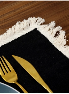 Macro shot of black linen placemat featuring bohemian fringe and premium texture