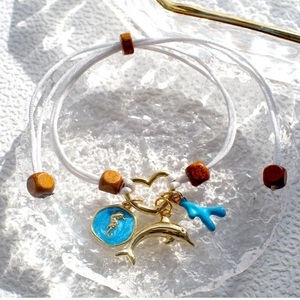 Detail of woven ocean bracelet with gold dolphin, seahorse charm and blue coral pendant