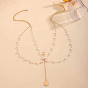 Detail of gold body chain with pearls and teardrop gemstone pendant on beige background