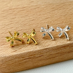 Macro detail of elegant gold and silver bow stud earrings on a textured wooden surface
