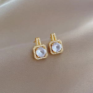 Macro shot of gold square stud earrings with clear zircon on champagne satin
