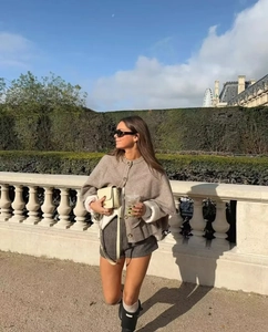 Outdoor street shot of grey knit cape shawl paired with checkered shorts and boots