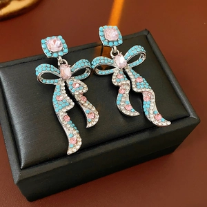 Détail de boucles d'oreilles nœud argentées avec pierres roses sur présentoir