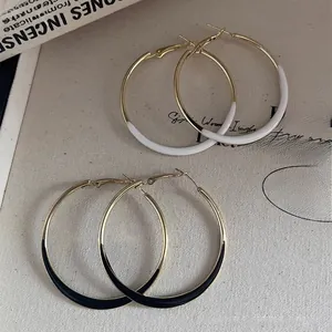 Detail of large gold hoop earrings with black and white enamel finish on textured background