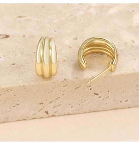 Detailed close-up of ribbed golden C-shape stud earrings on a textured stone surface