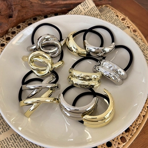 Close-up of minimalist gold and silver metal charms on black elastic hair ties in a tray