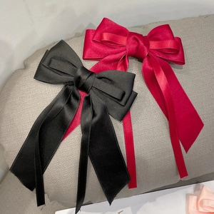 Detail showing elegant oversized satin bow hair clips with long ribbons in red and black