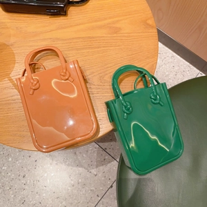 Close-up of orange and green PVC jelly handbags with knotted handles on a wooden table