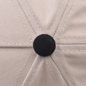 Dettaglio del bottone superiore del cappello in twill di cotone beige con cuciture precise