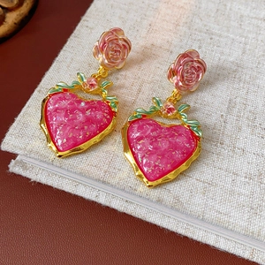 Close-up of vintage gold earrings with pink heart charms and delicate rose flower details