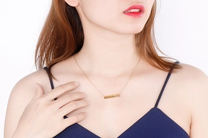 Close-up of golden bar pendant necklace with heart gemstone on a model's collarbone