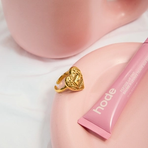 Macro detail of 18K gold-plated heart ring with embossed textures on a pink tray