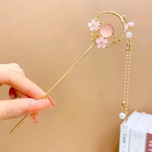 Detail of golden metal hair stick with pink flower and pearl tassel in hand