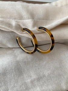 Close-up of C-shaped tortoiseshell resin earrings with gold trim on linen cloth