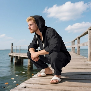 Men's loose black linen hoodie set with long pants shown on a beach boardwalk