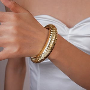 Close-up of a wide gold cuff bracelet featuring bold ridged textures on model wrist