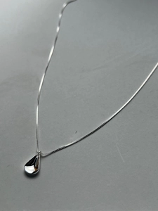 Macro detail of high-polished S925 sterling silver water-drop pendant on fine box chain