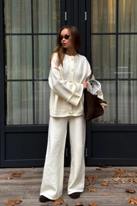 Detail of warm white knit cardigan and wide-leg pants set on an autumn wooden deck