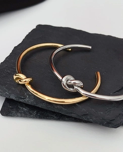 Detail of gold and silver knot bangles on a stone base showing high-gloss metallic finish