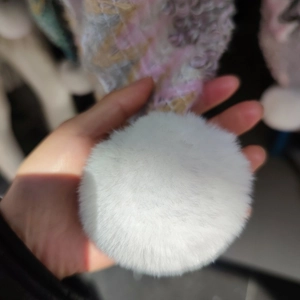 Close-up of fluffy white faux fur pom-pom detail on a knit ethnic style cape shawl