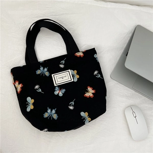 Détail d'un sac cabas en toile noire avec broderie papillon à côté d'un ordinateur