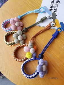 Detail of colorful woven flower phone lanyards with metal clasps on a wood surface