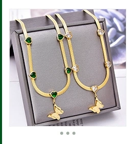Detail of gold snake chain necklace featuring butterfly pendant and green heart zircon