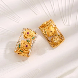 Close-up of golden hollow rectangular earrings with 3D roses and colorful gemstones