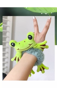 Detailed view of a plush green frog hair tie worn on a wrist as a soft bracelet