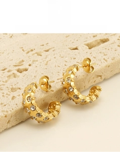 Macro shot of 18K gold plated C-shaped earrings with rhinestones on stone background