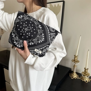 Close-up of black paisley canvas makeup bag held by a model in a cozy indoor setting