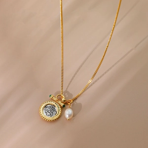Detail of vintage gold necklace featuring a coin pendant, baroque pearl, and toggle clasp