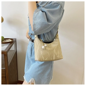 Beige underarm bag with glossy crinkled texture and bead detail on a model