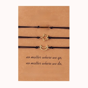 Close-up of three woven friendship bracelets with sun moon and star charms on a card