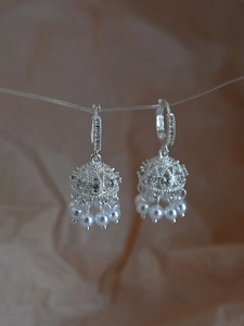 Detail of silver jhumka earrings with zircon pavé and white pearl tassels on brown background
